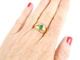 woman ' s hand with red manicured nails and a gold ring with a green stone