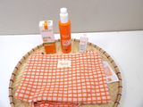 an orange and white towel, a bottle of sunscreen, and a bottle of sunscreen on a wicker tray