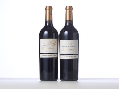 two bottles of red wine sitting on top of a white table