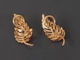 a pair of gold earrings with leaves on them on a black background