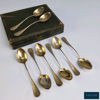 six cuillères et une boîte de couverts sont posés sur une table