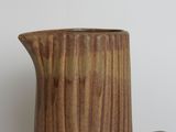 a brown pitcher sitting on a table with a white wall in the background