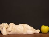 a statue of an angel laying on a table next to an apple