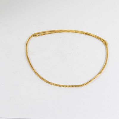 un collier à chaîne en or posé sur une surface blanche