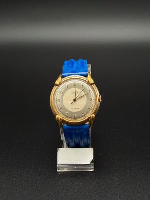 une image représentant une montre dorée et bleue posée sur une surface noire