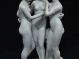 deux statues blanches représentant trois femmes se tenant par la main, posées sur un fond noir