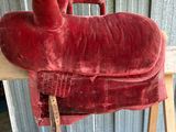 une selle de cheval rouge posée sur un banc en bois