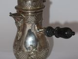une théière en argent avec une anse noire posée sur une table