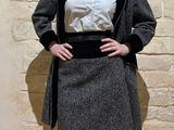a woman standing in front of a wall wearing a skirt and jacket