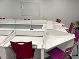 des tables et des chaises dans une salle de classe avec un tableau blanc accroché au mur