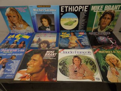 plusieurs pochettes d'albums différentes posées sur une table, avec un homme en arrière-plan