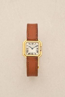 a close up of a watch on a white surface with a brown strap
