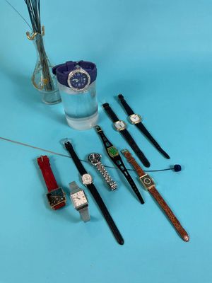 several different watches and a vase of flowers on a blue surface