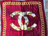 a close up of a red scarf with a gold chain and a chanel logo