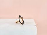 une bague en or sertie de diamants noirs repose sur un bloc de marbre