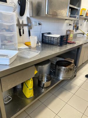 un plan de travail en acier inoxydable sur lequel sont posés des casseroles et des poêles, dans une cuisine professionnelle