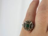 an image of a woman ' s hand holding a ring with a green stone on it