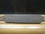 une plaque posée sur un rebord de fenêtre sur laquelle on peut lire « Monsieur Léon Dubbos »