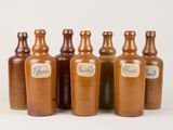 six bouteilles marron munies d'étiquettes sont alignées en rangée