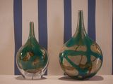two glass vases sitting on a table with a striped wall behind them