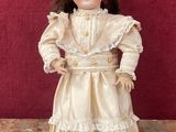 une poupée ancienne représentant une jeune fille vêtue d'une robe blanche et de chaussures noires
