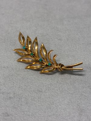 a close up of a gold leaf brooch with green stones