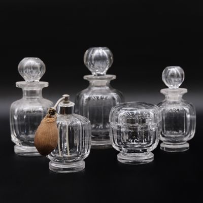 six bouteilles en verre transparent munies de bouchons en bois, posées sur un support noir