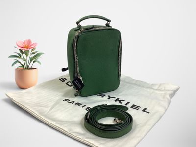 le petit sac vert est posé sur une nappe blanche, à côté d'une fleur rose