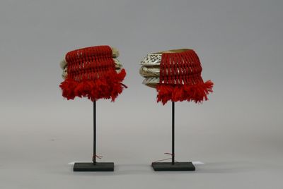 pair of red and white hats with feathers on stands on a white surface