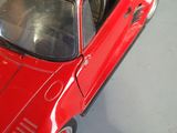 a hand holding a red toy car with a black roof