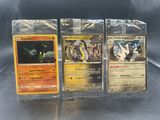 Trois cartes Pokémon sont posées sur une table devant un fond noir.