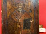 an old wooden icon of a man holding a book on a red wall