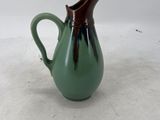 a green pitcher with a brown handle on a white surface