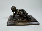 bronze statue of a boy laying on his stomach on a wooden base