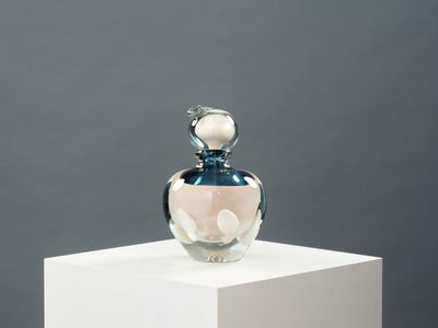 une bouteille en verre surmontée d'une fleur, posée sur un socle blanc