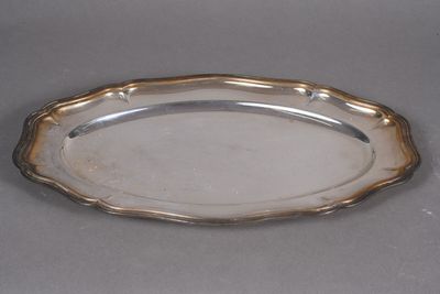 an antique silver plate with a decorative edge on a gray surface