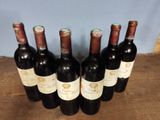 six bottles of wine are lined up on a wooden table