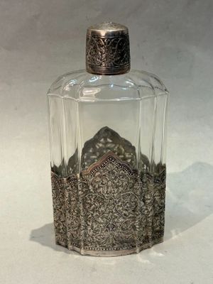 une bouteille en verre avec un bouchon argenté posée sur une surface blanche