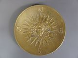 une médaille d'or sur laquelle est représenté un soleil, posée sur un fond blanc
