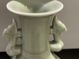 a white vase with a green handle on a table