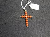 an orange beaded cross hangs from a silver chain on a black surface