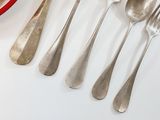 a lot of silverware on a table with a bowl of strawberries in the background