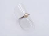 a white pearl and silver ring sitting on top of a clear glass