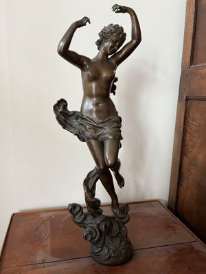 statue en bronze représentant une femme tenant un oiseau, posée sur une table en bois