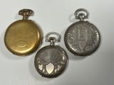 trois montres de poche en argent et en or sont posées sur une surface blanche