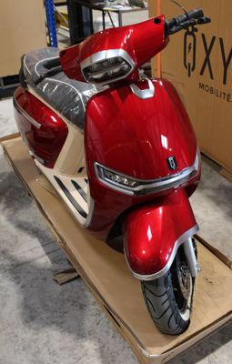 un scooter rouge posé sur un chariot devant une boîte
