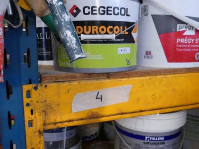 Plusieurs seaux de peinture sont empilés sur une étagère dans un garage