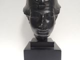 une sculpture noire représentant la tête d'une femme coiffée d'un casque