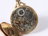 a gold pocket watch with gears inside of it on a white surface