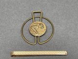 a close up of a gold tie bar with a coin on it
